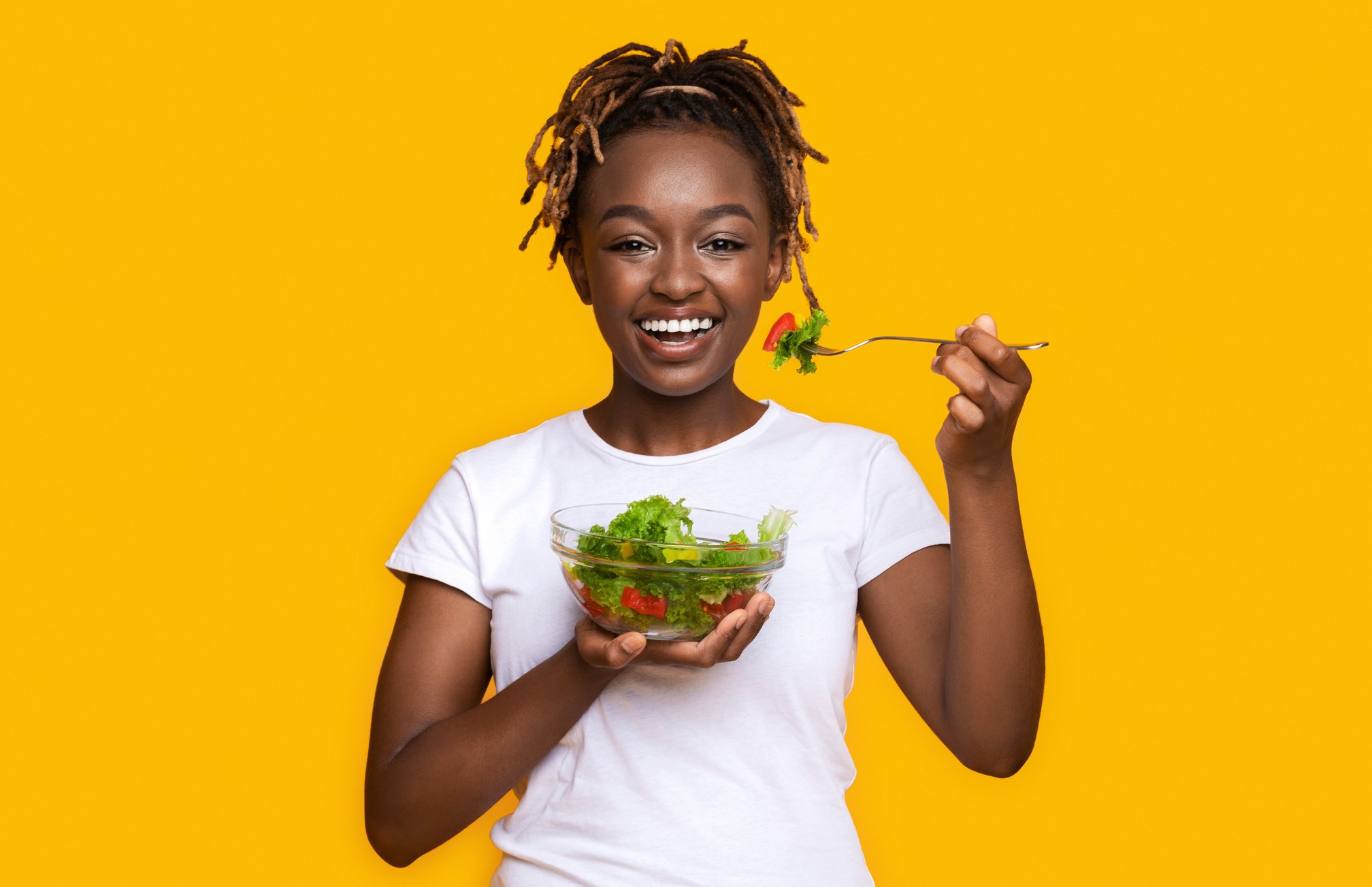 Healthy black girl eating fresh salad over yellow